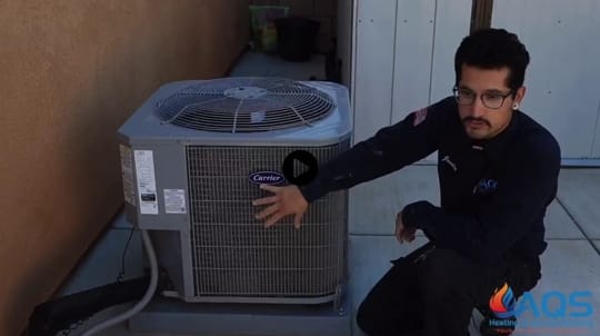 Technician from AQS Heating & Air Conditioning demonstrating air conditioning unit maintenance beside Carrier AC unit, emphasizing emergency repair services for HVAC systems.