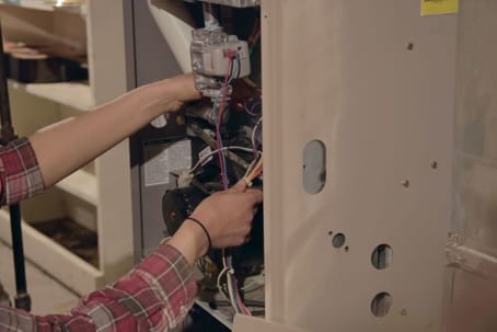 Person troubleshooting a furnace, inspecting internal components and wiring, in a residential setting, relevant to HVAC maintenance and repair services.