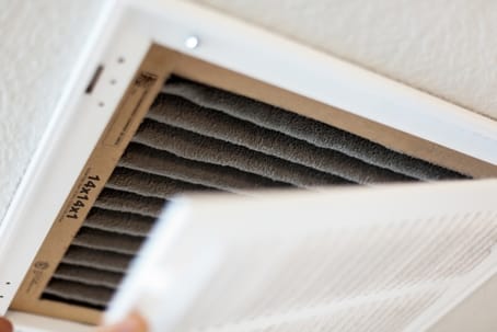 Dirty air filter being removed from an HVAC system, illustrating the importance of regular maintenance for improved indoor air quality and efficient air conditioning performance.