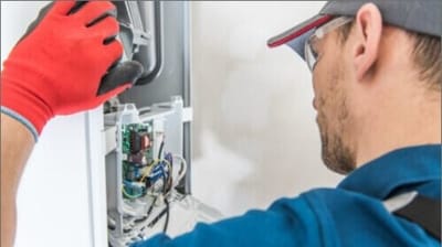Technician in red gloves inspecting the internal components of an air conditioning unit, emphasizing maintenance and repair services related to heating and cooling systems.