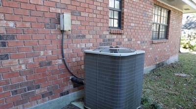 Ductless mini-split air handler unit installed outside a brick home, illustrating HVAC system components related to maintenance and repair services offered by AQS Heating and Air Conditioning.