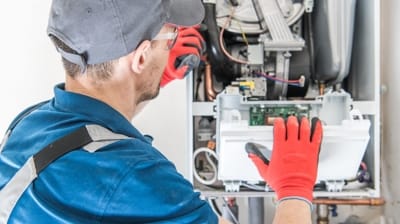 A local HVAC repair technician in a blue uniform and red gloves meticulously inspects and repairs an industrial appliance, ensuring optimal performance.