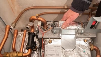 Technician inspecting heat pump components, focusing on copper pipes and electrical connections, relevant to heating repair services in Hemet, CA.