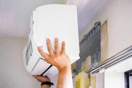 A professional from Hemet is performing AC maintenance by installing or removing a wall-mounted air conditioning unit indoors.