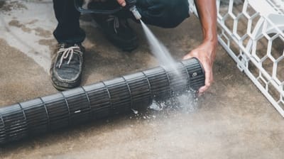 Person cleaning air conditioning coils with a pressure washer, emphasizing maintenance and efficiency for HVAC systems.
