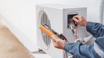 Technician using a multimeter to diagnose an outdoor air conditioning unit, highlighting HVAC maintenance and troubleshooting for efficient cooling systems.