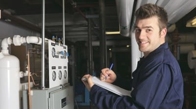 HVAC technician inspecting a commercial heating system and taking notes for maintenance at AQS Heating & Air Conditioning.