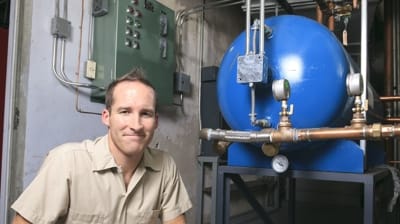 Technician posing next to a large blue heating tank and control panel, emphasizing HVAC maintenance and inspection services.