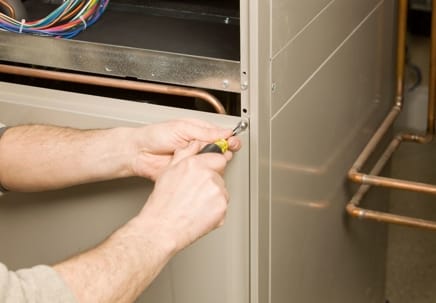 Hands using a screwdriver to install a gas furnace, highlighting the installation process essential for homeowners considering furnace installation.