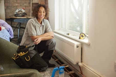 Smiling HVAC technician beside a radiator, showcasing tools and equipment for heating system maintenance and repair.