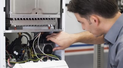 Technician in Hemet, California inspecting and adjusting internal components of an open equipment unit, performing essential AC maintenance.