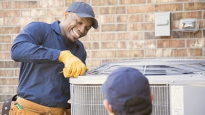 HVAC technician smiling while servicing outdoor air conditioning unit, emphasizing professional maintenance and care for home comfort.