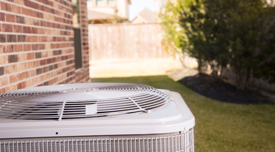Air conditioning unit outdoors near brick wall, emphasizing importance of annual maintenance for efficient summer cooling.