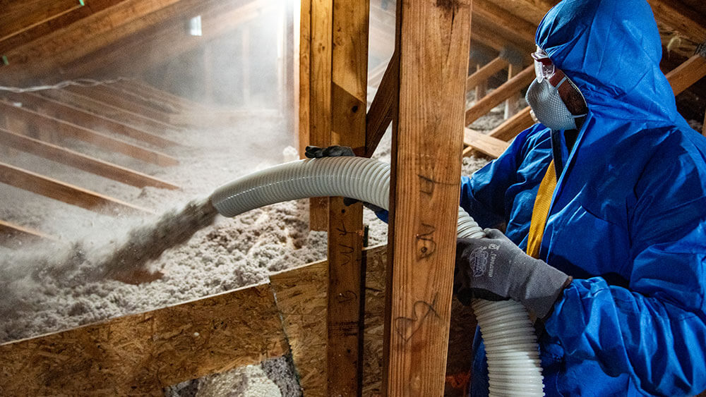 Worker installing blown-in cellulose insulation in attic, enhancing energy efficiency and comfort in homes.